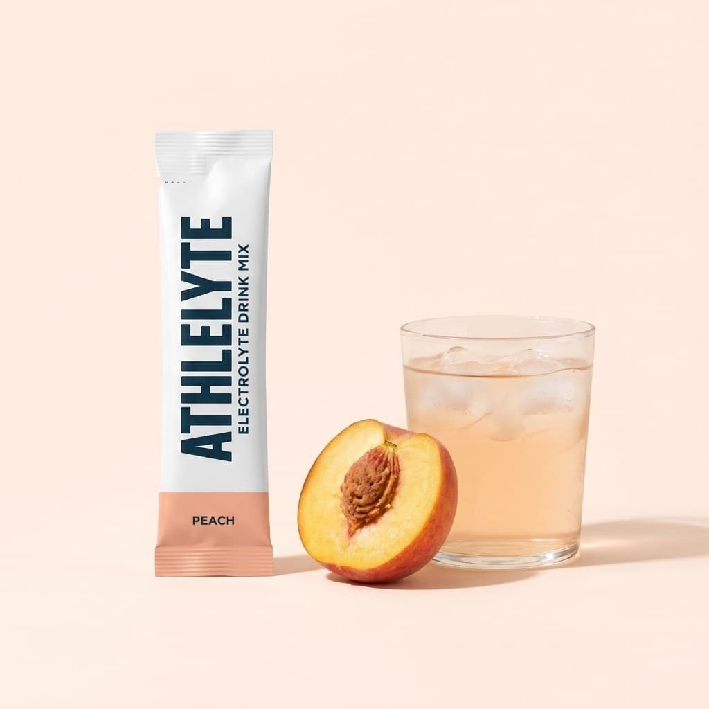 Athlelyte Peach stick pack beside a halved peach and a glass of pale peach water