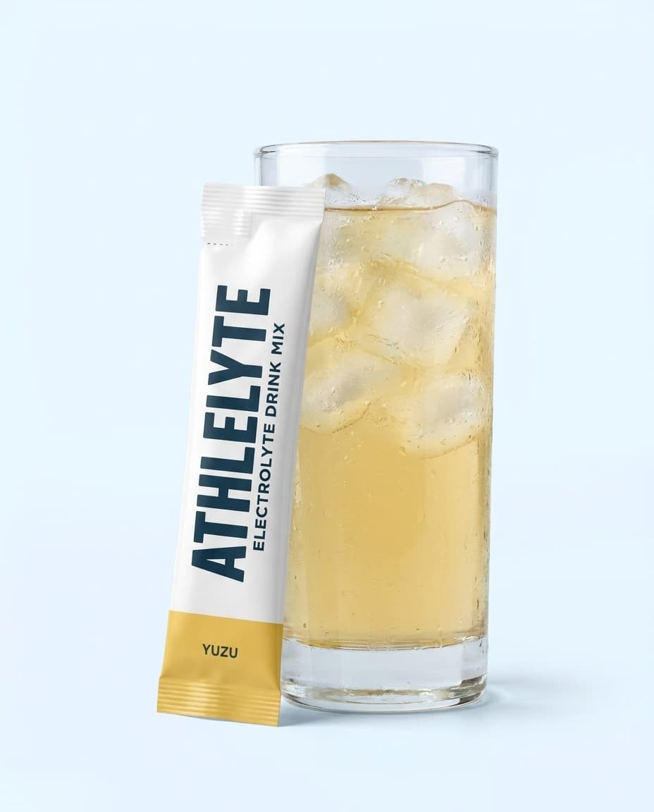 Athlelyte Yuzu electrolyte stick pack standing beside a tall glass of pale golden yuzu water with ice